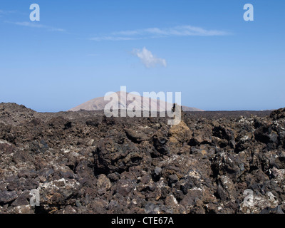 Lava-campo con taglienti rocce irregolari e un vecchio vulcano sullo sfondo vicino Timanfaya in Lanzarote Foto Stock