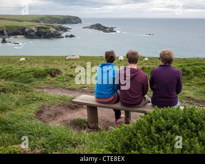 Tre persone sedute su una panchina di fronte al mare nella parte superiore di scogliere a Porthcothan baia vicino a Padstow Cornwall Regno Unito Foto Stock