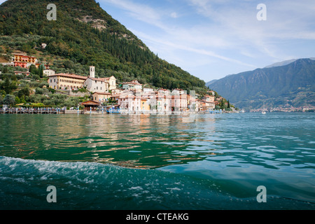 Comune di Peschiera, Monte Isola, visto dalla barca da Sulzano, con la ripida collina alle spalle e la riflessione in acqua. Foto Stock