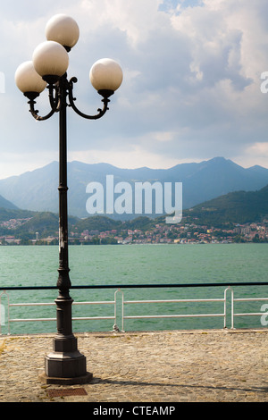 Lampione e lago-lato promenade a Pisogne con vista in lontananza Lovere attraverso il Lago d'Iseo, montagne, nuvole edificio. Foto Stock