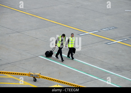 Pilota e copilota a piedi attraverso il grembiule con i bagagli, Birmingham Airport, West Midlands, Inghilterra, Regno Unito, Europa occidentale. Foto Stock