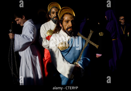 Un uomo mascherato vestito come un personaggio biblico contiene una croce durante una PASQUA SETTIMANA SANTA PROCESSIONE in Puente Genil, Spagna Foto Stock
