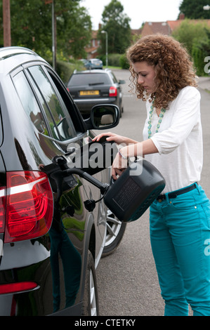 Donna conducente il riempimento della macchina il serbatoio del combustibile con gasolio da un colorato di nero può su strada Foto Stock