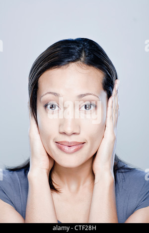 Ritratto di giovane donna con le mani che coprono le orecchie, studio shot Foto Stock