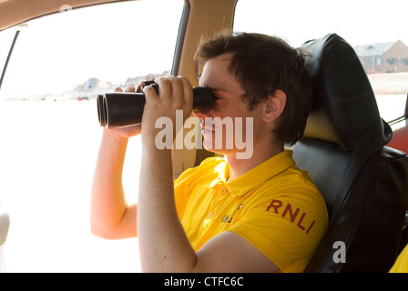 Bagnino RNLI rilievi del litorale attraverso il suo binocolo Foto Stock