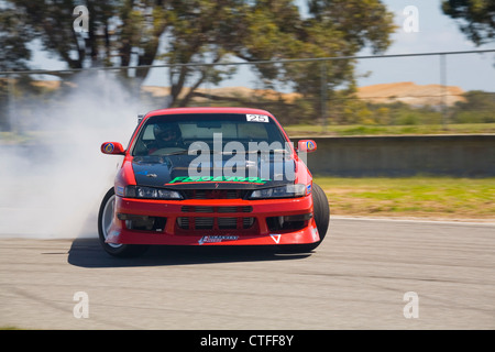 Una deriva motorsport vettura scivolare lateralmente con fumo di pneumatici in un angolo durante una competizione di drifting. Foto Stock