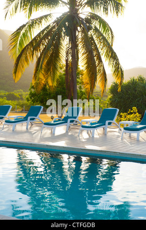 Caribbean West Indies Nevis Mount Nevis Hotel piscina relax tropicale sedie a sdraio al tramonto attraverso le palme Foto Stock