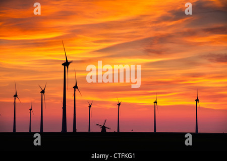 I Paesi Bassi, Eemsmond, Eemshaven, Windturbines e mulino a vento tradizionale. Il tramonto. Foto Stock