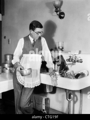 1920s UOMO IN grembiule appoggiata sul lavello pieno di piatti sporchi RAG IN UNA MANO il POT IN ALTRI Foto Stock