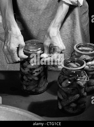 Anni Cinquanta close-up di donna anziana con le mani in mano il coperchio di tenuta su un vasetto di fatti in casa a base di sottaceti Foto Stock