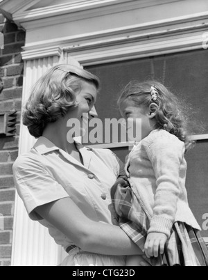 Anni Cinquanta madre TENENDO LA FIGLIA DI ARMI a sorridere a lei nella porta al di fuori della propria casa Foto Stock