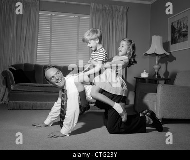 Anni Cinquanta anni sessanta papà che trasportano Boy & GIRL PIGGYBACK SULLA VITA IL PAVIMENTO DELLA CAMERA Foto Stock