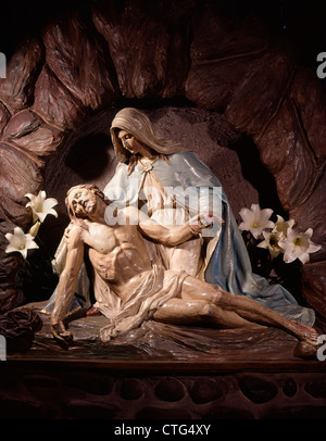 Una pietà statua di Maria Madre tenendo il corpo morto di Gesù Cristo nel suo grembo con gigli bianchi Foto Stock