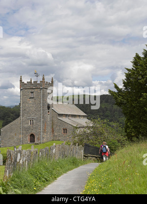 Persone a piedi alla chiesa parrocchiale del 15 ° secolo di San Michele E tutti gli Angeli in estate Hawkshead Village Cumbria Inghilterra UK Regno Unito Gran Bretagna Foto Stock