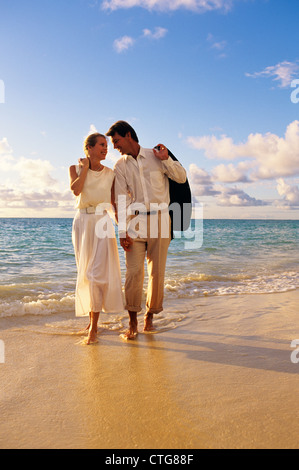 Anni ottanta anni novanta giovane camminando sulla spiaggia donna che indossa abito bianco pantaloni uomo Giacca SULLA SPALLA GUARDANDO OGNI ALTRO Foto Stock