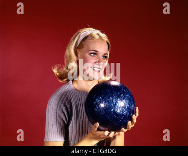 Anni sessanta giovane donna bionda tenendo palla da bowling sport retrò che indossa un maglione blu Foto Stock