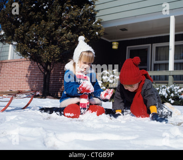 Anni Settanta due bambini giocare nella neve con una slitta nel cortile anteriore Foto Stock