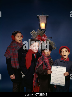Anni sessanta gruppo bambini Boys Singing canti di Natale sotto lampada posta retrò diversità etnica multi-etnico mix razziali Foto Stock
