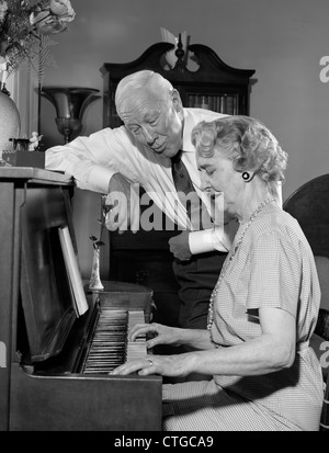 Anni sessanta donna anziana suonare il pianoforte con mio marito in piedi accanto al suo canto Foto Stock