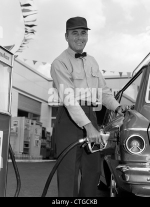 Anni sessanta maschi stazione di servizio operatore che indossa il cappello e il filtro Bow Tie sorridente mentre pompando benzina al di fuori Foto Stock