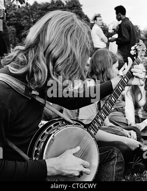 Anni Settanta VISTA LATERALE DI HIPPIE TEEN raccolta esterna con con i capelli lunghi BOY in primo piano la riproduzione di musica bluegrass banjo Foto Stock