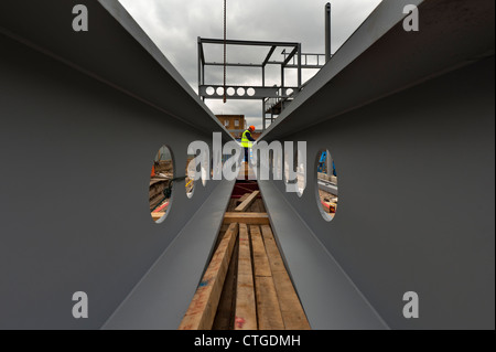 Travi nel cantiere edile, con operatore che si prepara a controllare il paranco di due grandi travi metalliche Foto Stock