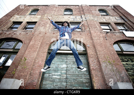 Uomo nero jumping accanto al palazzo urbano Foto Stock