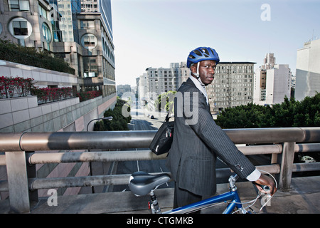 Imprenditore bicicletta spinta oltre il ponte urbano Foto Stock