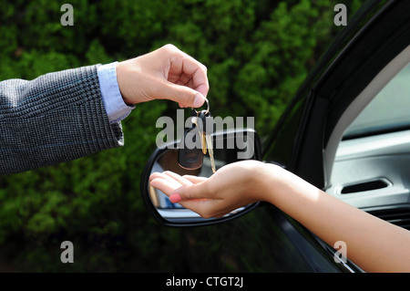 Venditore di consegnare le chiavi di una nuova vettura. Primo piano della mano d'uomo di consegnare le chiavi per la donna incollaggio a mano fuori dalla finestra Foto Stock