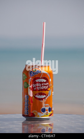 Gusterete una lattina di arancia Fanta sul mare a Weymouth, Dorset UK a maggio - bevande lattina con paglia di plastica Foto Stock