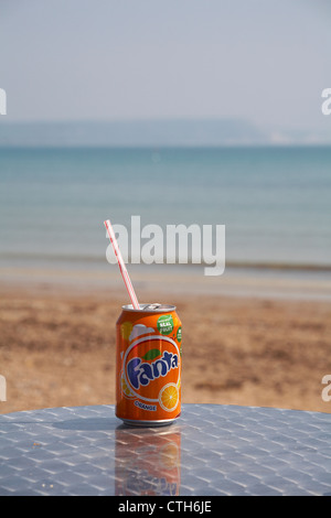 Gusterete una lattina di arancia Fanta sul mare a Weymouth, Dorset UK a maggio - bevande lattina con paglia di plastica Foto Stock