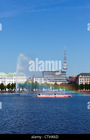 Imbarcazione turistica passando la fontana sul lago Binnenalster a Amburgo, rainbow nella spruzzatura di acqua Foto Stock