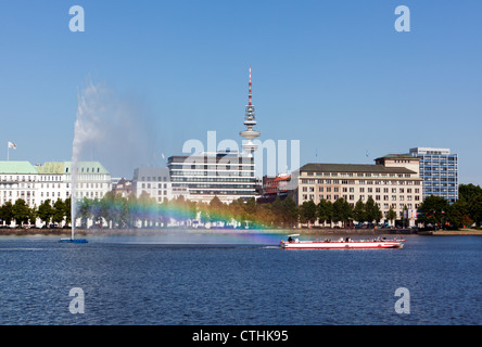 Imbarcazione turistica passando la fontana sul lago Binnenalster a Amburgo, rainbow nella spruzzatura di acqua Foto Stock