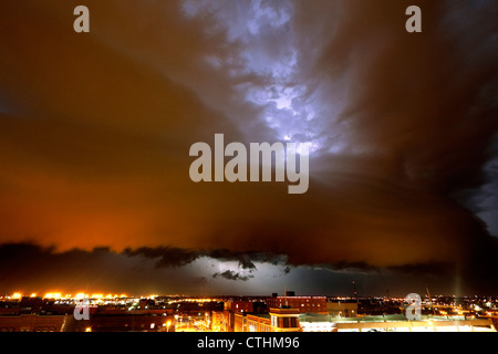 Un fungo-capped conformato temporale arcus cloud si sposta al di sopra di una città, illuminato da un fulmine. Foto Stock