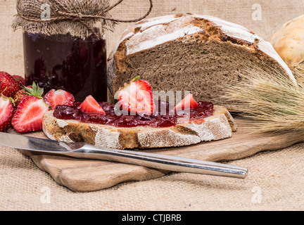 Fatta fresca Confettura di fragole sul pane con frutti su sfondo rustico Foto Stock