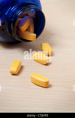 Bottiglia blu di giallo vitamina pillole con alcuni fuoriuscita sul tavolo Foto Stock