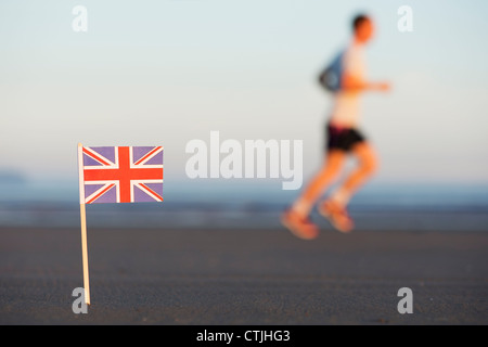 L'uomo jogging passato un Union Jack flag bloccato in una spiaggia a sunrise. Messa a fuoco selettiva Foto Stock
