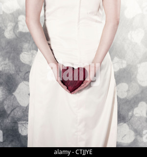 Una ragazza in un abito bianco tenendo un cuore nelle sue mani Foto Stock