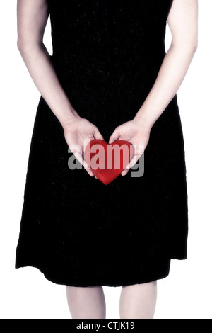 Una ragazza in un abito nero tenendo un cuore rosso dietro la schiena Foto Stock