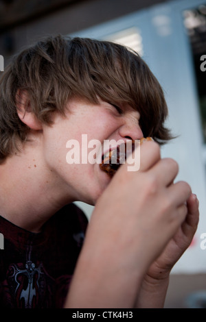 Tredici anni ragazzo affamato morde un pezzo di pollo alla brace. Foto Stock