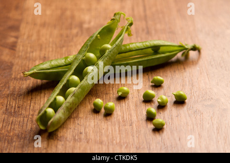 Due open baccelli di piselli con alcuni allentati i piselli, posto su un sfondo di legno Foto Stock