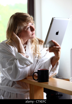 Giovane donna è utilizzando un IPad, tablet PC, la navigazione in Internet tramite connessione wireless, al mattino, avente una tazza di caffè Foto Stock