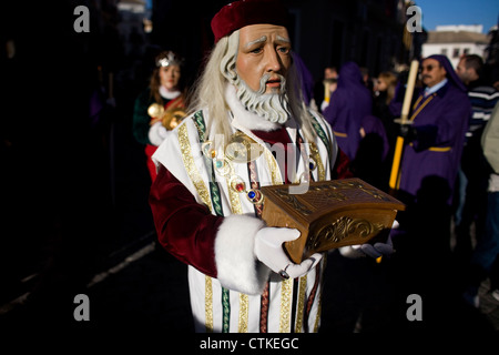Un uomo mascherato vestito come un personaggio biblico contiene una scatola di legno durante una PASQUA SETTIMANA SANTA PROCESSIONE in Puente Genil, Spagna Foto Stock