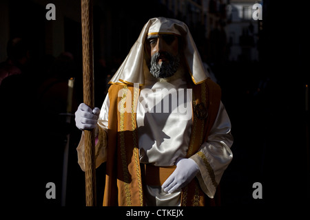Un uomo mascherato vestito come un personaggio biblico cammina con una personale durante una PASQUA SETTIMANA SANTA PROCESSIONE in Puente Genil, Spagna Foto Stock