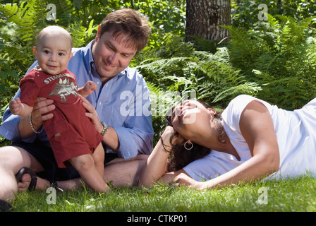 Un multi etnico famiglia appendere fuori sul prato con il loro bambino. Foto Stock