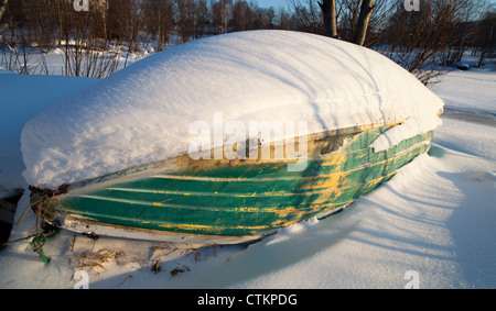 Neve coperta vecchio logoro fiberglass isolato rowboat / skiff. In bretata a Winter , Finlandia Foto Stock