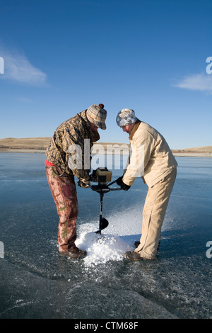 Un padre e figlio in team su una coclea di alimentazione di trapanare i fori per la pesca sul ghiaccio. Foto Stock