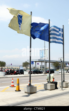 Le bandiere della Grecia la UE e dall'aeroporto di Atene volare al di fuori del terminal arrivi, orientamento verticale Foto Stock