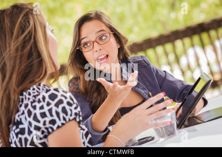 Attraente razza mista ragazze sorridenti e parlare mentre si lavora sul computer Tablet seduti all'aperto. Foto Stock