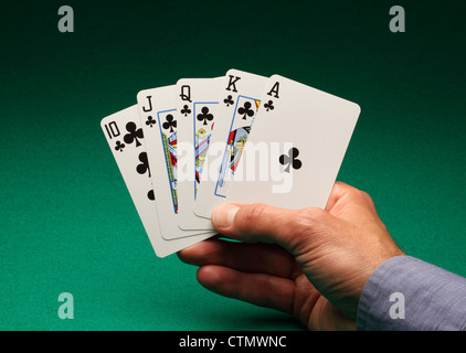 Una mano d'uomo azienda carte da gioco su un tavolo verde. Un Royal Flush di club nel gioco del Poker Foto Stock